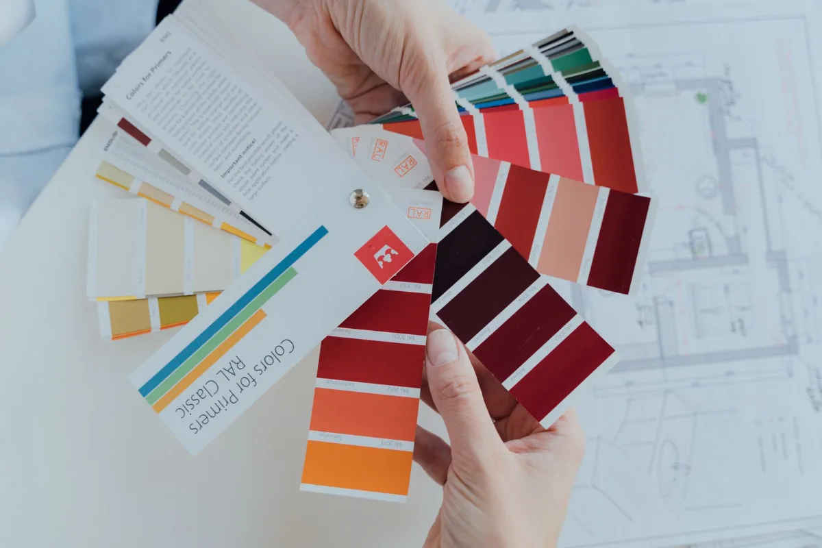 A printed color spec sheet with vinyl swatches and Pantone chips taped beside the on-screen hex values
