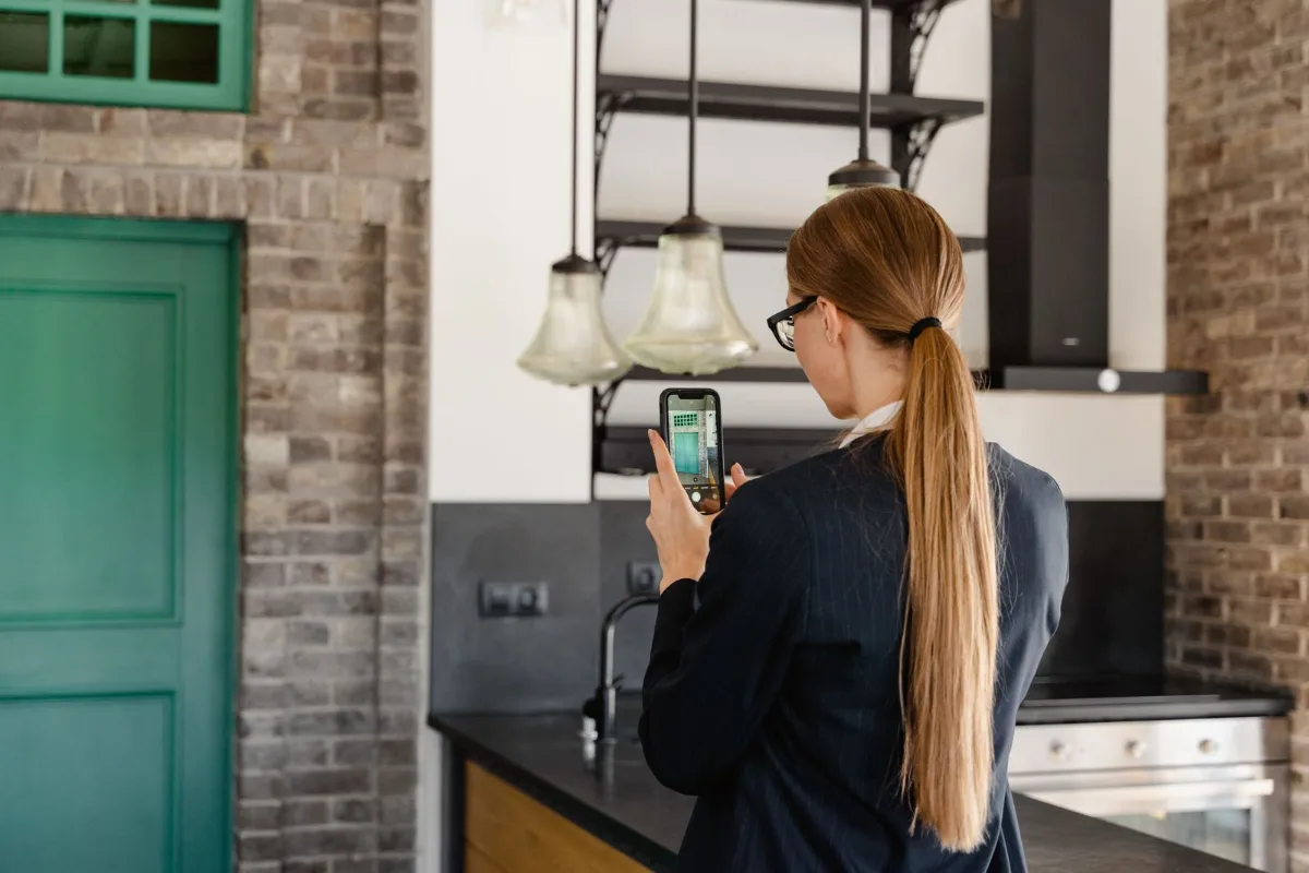A homeowner standing in a hallway holding a phone up to a thermostat that reads 84 degrees
